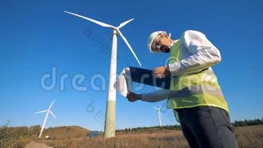在风力涡轮机附近<strong>行走</strong>时，<strong>一个人</strong>拿着<strong>一</strong>个剪贴板。 可再生电能，绿色能源概念。